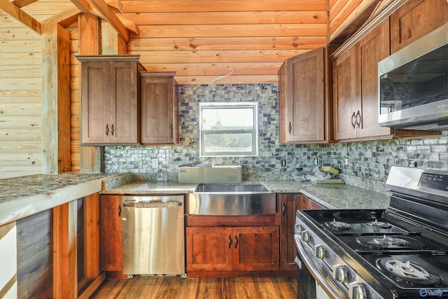 kitchen with light stone countertops, appliances with stainless steel finishes, decorative backsplash, dark wood-type flooring, and wood walls