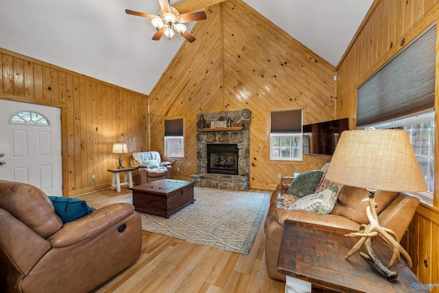 living room with light hardwood / wood-style flooring, a stone fireplace, ceiling fan, high vaulted ceiling, and wooden walls