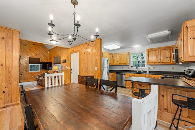 kitchen with light wood-type flooring, stainless steel appliances, decorative light fixtures, sink, and wooden walls