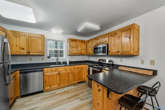 kitchen with appliances with stainless steel finishes, a kitchen breakfast bar, light wood-type flooring, sink, and kitchen peninsula