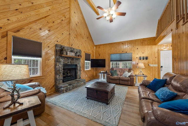 living room with high vaulted ceiling, wood walls, a stone fireplace, and light hardwood / wood-style flooring