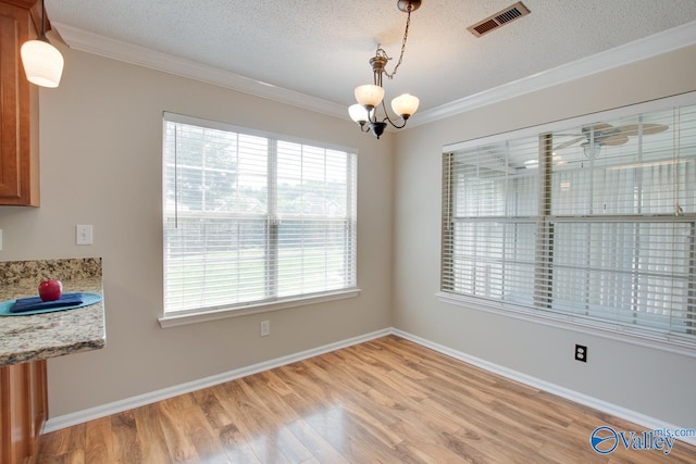 unfurnished dining area featuring plenty of natural light, a chandelier, crown molding, light wood-style flooring, and a textured ceiling