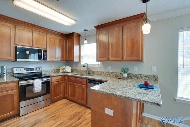 kitchen with appliances with stainless steel finishes, a sink, crown molding, a peninsula, and light wood-type flooring