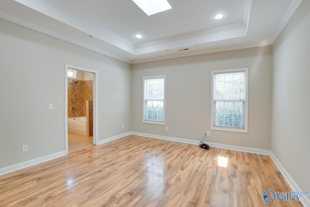 unfurnished room featuring crown molding, light wood-type flooring, a raised ceiling, a skylight, and recessed lighting