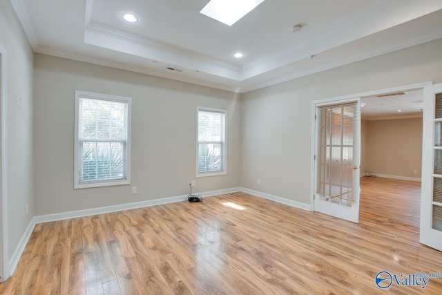 spare room with crown molding, light wood finished floors, a raised ceiling, baseboards, and a smoke detector