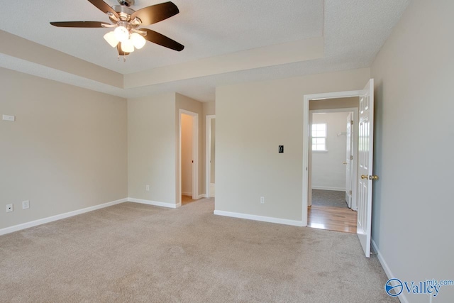 empty room with light carpet, a ceiling fan, baseboards, and a tray ceiling