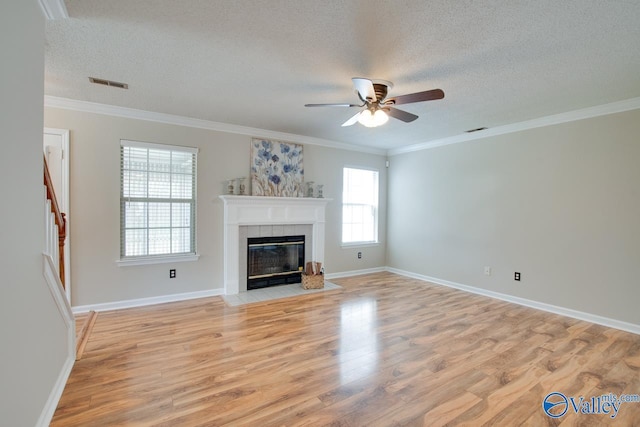 unfurnished living room featuring ceiling fan, light wood-style flooring, a textured ceiling, a tiled fireplace, and stairs