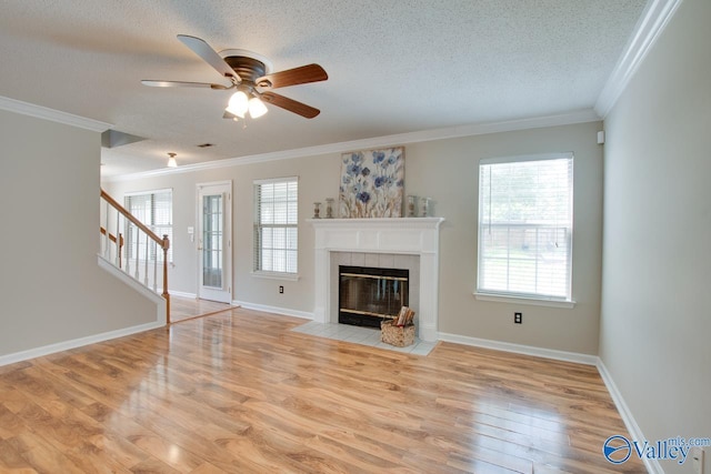 unfurnished living room with a textured ceiling, ceiling fan, light wood-style flooring, stairway, and a tile fireplace