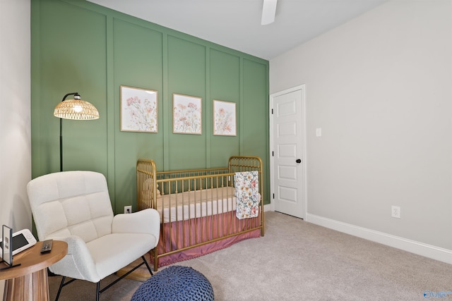 bedroom featuring a decorative wall, a nursery area, ceiling fan, carpet floors, and baseboards