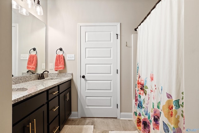 full bath featuring double vanity, a shower with shower curtain, baseboards, and a sink