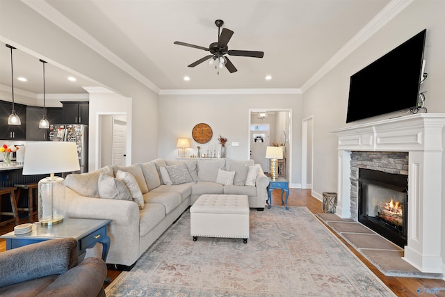living room with a ceiling fan, recessed lighting, a stone fireplace, crown molding, and light wood-style floors