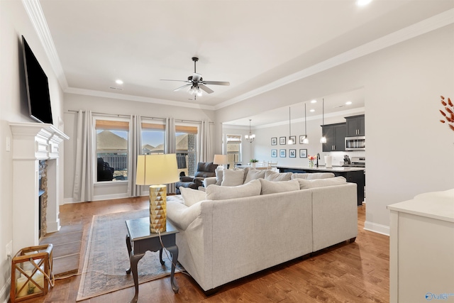 living room featuring crown molding, light wood-style floors, ceiling fan with notable chandelier, and recessed lighting