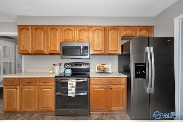 kitchen featuring stainless steel appliances, brown cabinets, light countertops, and a textured ceiling