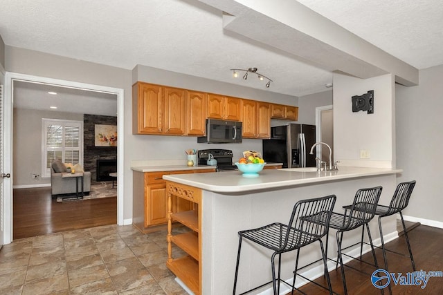 kitchen with a breakfast bar area, light countertops, a sink, stainless steel fridge, and black range with electric cooktop