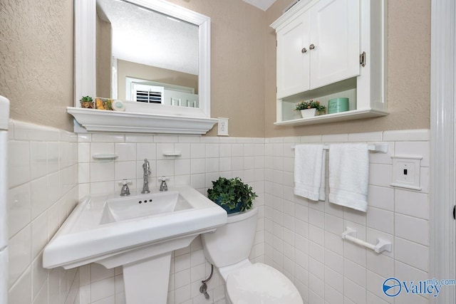 half bathroom with a wainscoted wall, a textured wall, toilet, and tile walls