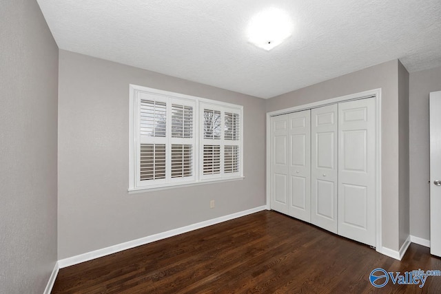 unfurnished bedroom with a textured ceiling, a closet, baseboards, and dark wood-style flooring