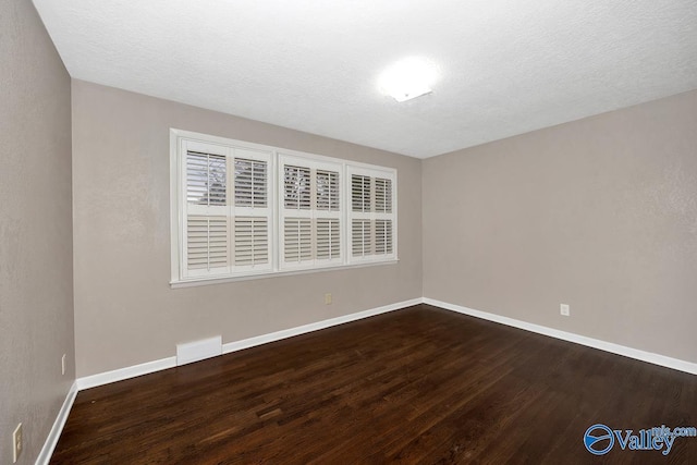 spare room featuring visible vents, a textured ceiling, baseboards, and wood finished floors