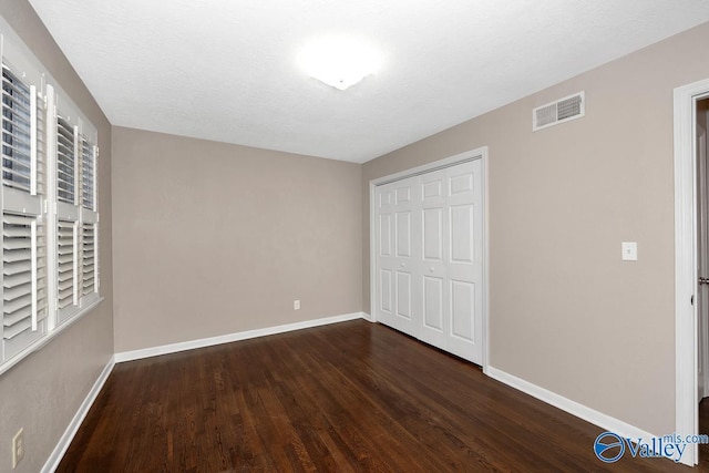 unfurnished bedroom with dark wood-style floors, a closet, visible vents, a textured ceiling, and baseboards