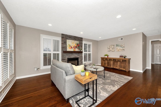 living room with a stone fireplace, wood finished floors, visible vents, and baseboards