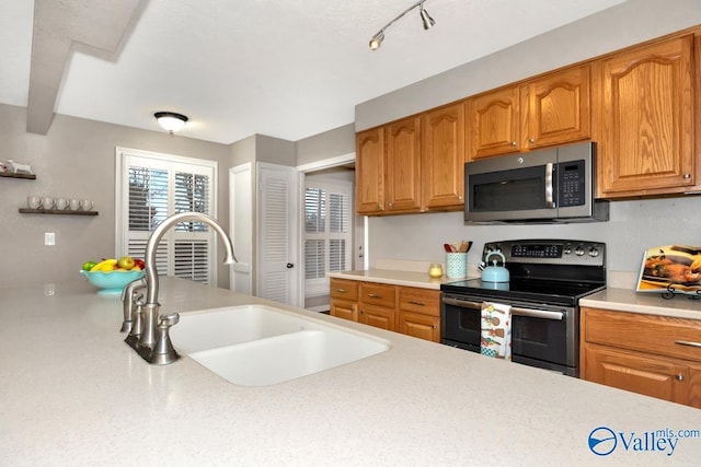 kitchen featuring brown cabinets, range with electric stovetop, light countertops, stainless steel microwave, and a sink