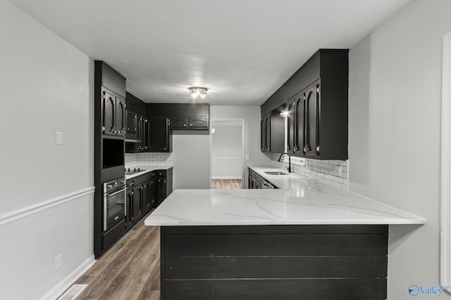 kitchen featuring kitchen peninsula, tasteful backsplash, stainless steel oven, black electric cooktop, and sink