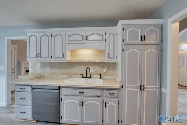 kitchen with tasteful backsplash, dishwashing machine, light wood-style floors, a textured ceiling, and a sink