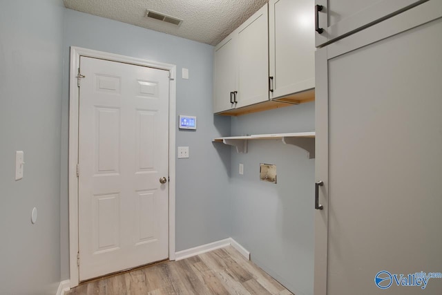 clothes washing area with visible vents, baseboards, light wood-type flooring, cabinet space, and a textured ceiling