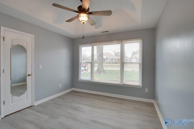 unfurnished room featuring a tray ceiling, baseboards, visible vents, and ceiling fan