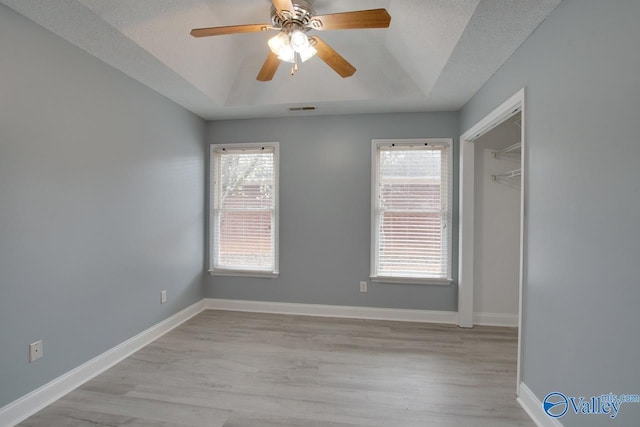 unfurnished room with plenty of natural light, light wood-style flooring, baseboards, and a tray ceiling