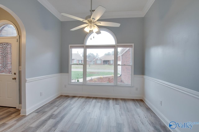 interior space with ceiling fan, arched walkways, ornamental molding, and light wood finished floors