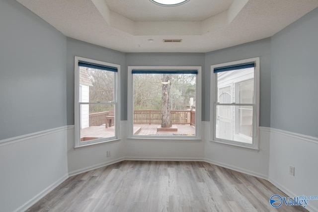 unfurnished room featuring visible vents, a raised ceiling, plenty of natural light, and wood finished floors