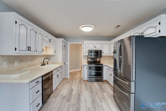 kitchen featuring light wood-style flooring, a sink, backsplash, stainless steel appliances, and light countertops