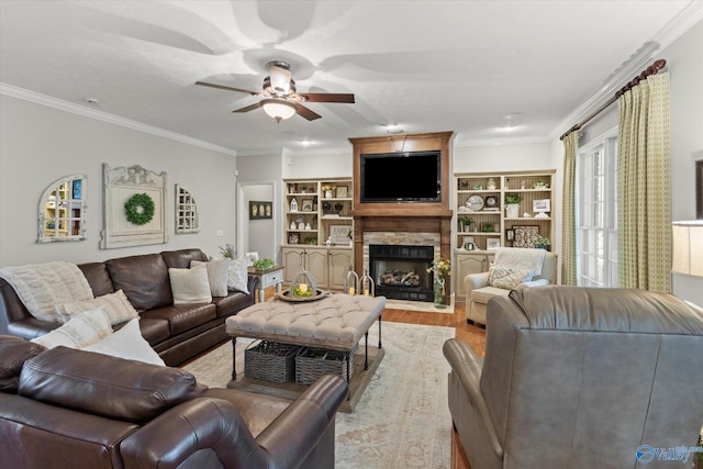 living room with crown molding, a stone fireplace, light hardwood / wood-style floors, and ceiling fan