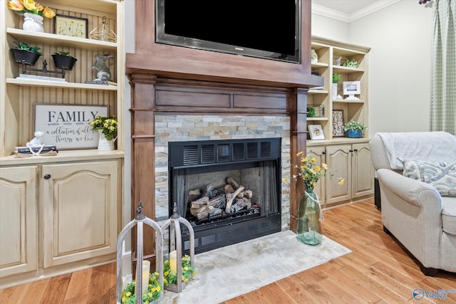 living room featuring crown molding, a stone fireplace, light wood-type flooring, and built in shelves