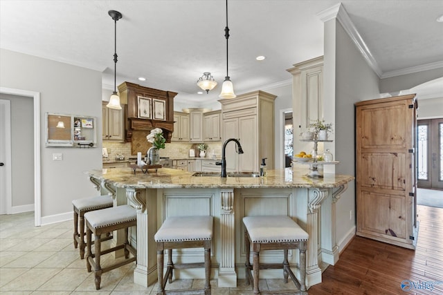 kitchen featuring sink, a breakfast bar area, backsplash, hanging light fixtures, and light stone countertops