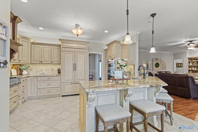 kitchen with a breakfast bar, sink, crown molding, hanging light fixtures, and cream cabinets