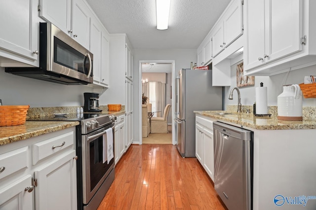 12501 S Shawdee Rd SE, Huntsville, AL 35803 - kitchen with appliances with stainless steel finishes, a sink, white cabinets, light wood-type flooring, and a textured ceiling