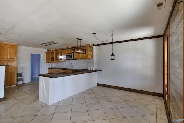 kitchen with dark countertops, a peninsula, a sink, glass insert cabinets, and stainless steel microwave