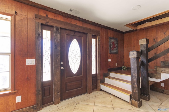 entrance foyer with light tile patterned flooring, stairway, wood walls, and visible vents