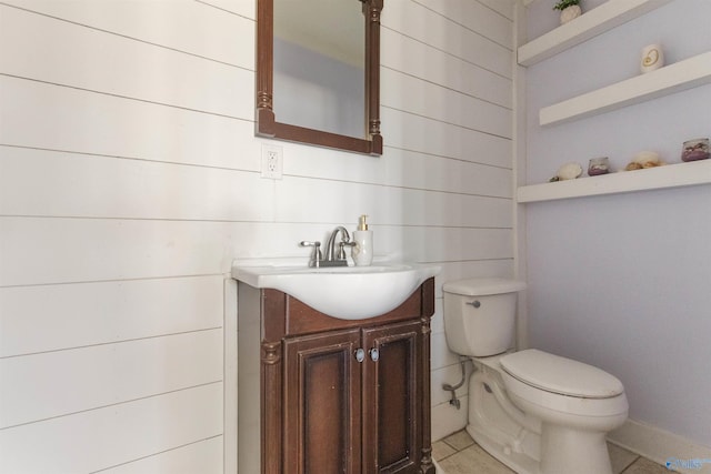 half bathroom featuring tile patterned floors, wooden walls, toilet, and vanity