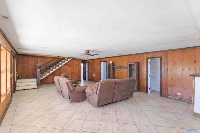 living area with wooden walls, stairway, a ceiling fan, and visible vents