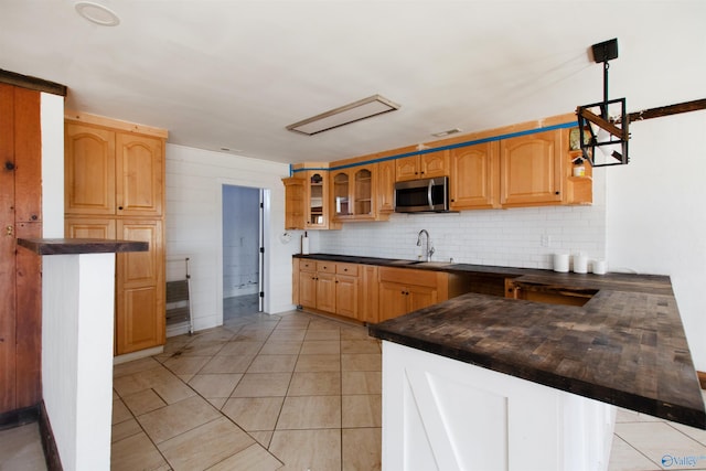 kitchen featuring dark countertops, a peninsula, decorative backsplash, glass insert cabinets, and stainless steel microwave