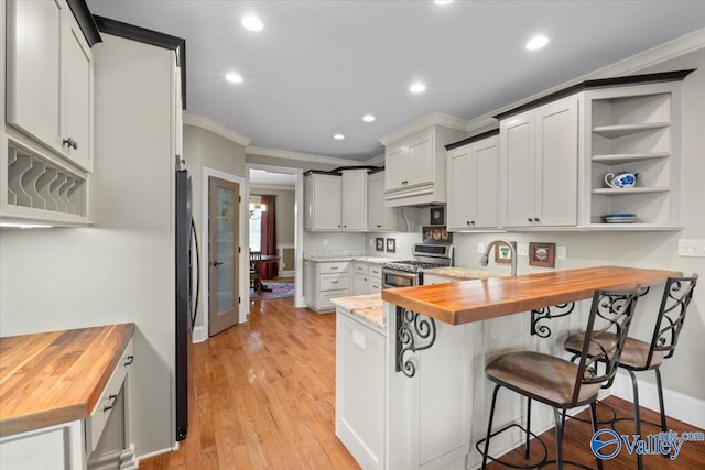 kitchen featuring crown molding, a kitchen bar, a peninsula, stainless steel gas range, and butcher block countertops