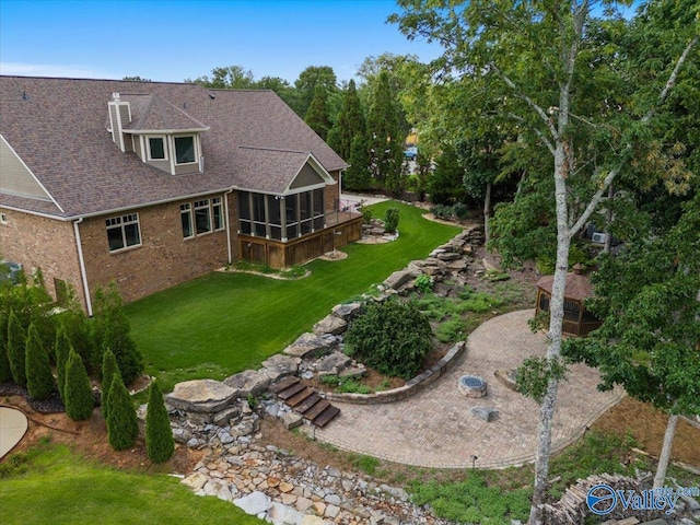 rear view of property with a shingled roof, a sunroom, a lawn, a chimney, and brick siding