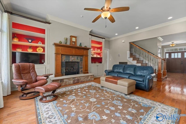living room featuring ornamental molding, a fireplace, stairway, ceiling fan, and hardwood / wood-style flooring