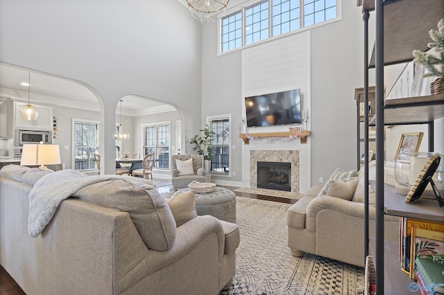 living room with a tiled fireplace, plenty of natural light, crown molding, and a chandelier