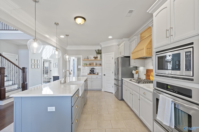 kitchen with premium range hood, appliances with stainless steel finishes, decorative light fixtures, white cabinets, and a center island with sink