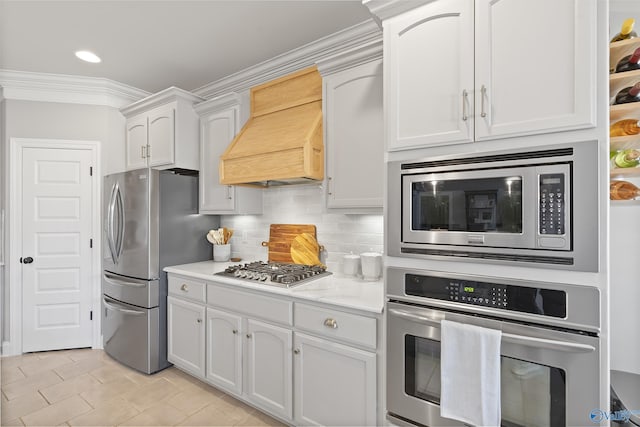 kitchen featuring appliances with stainless steel finishes, white cabinets, backsplash, ornamental molding, and custom range hood