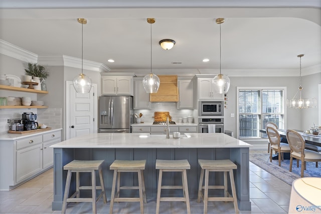 kitchen with appliances with stainless steel finishes, pendant lighting, custom exhaust hood, a kitchen island with sink, and crown molding