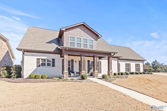 craftsman inspired home with a porch, a shingled roof, and brick siding